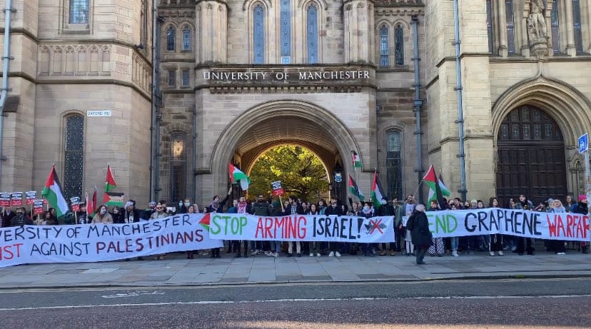 A rally in front of the Whitworth Arches, fancy old arches with "University of Manchester" above them. People are holding Palestine flags and banners reading "University of Manchester racist against Palestinians", "Stop arming Israel" and "End Graphene Warfare"